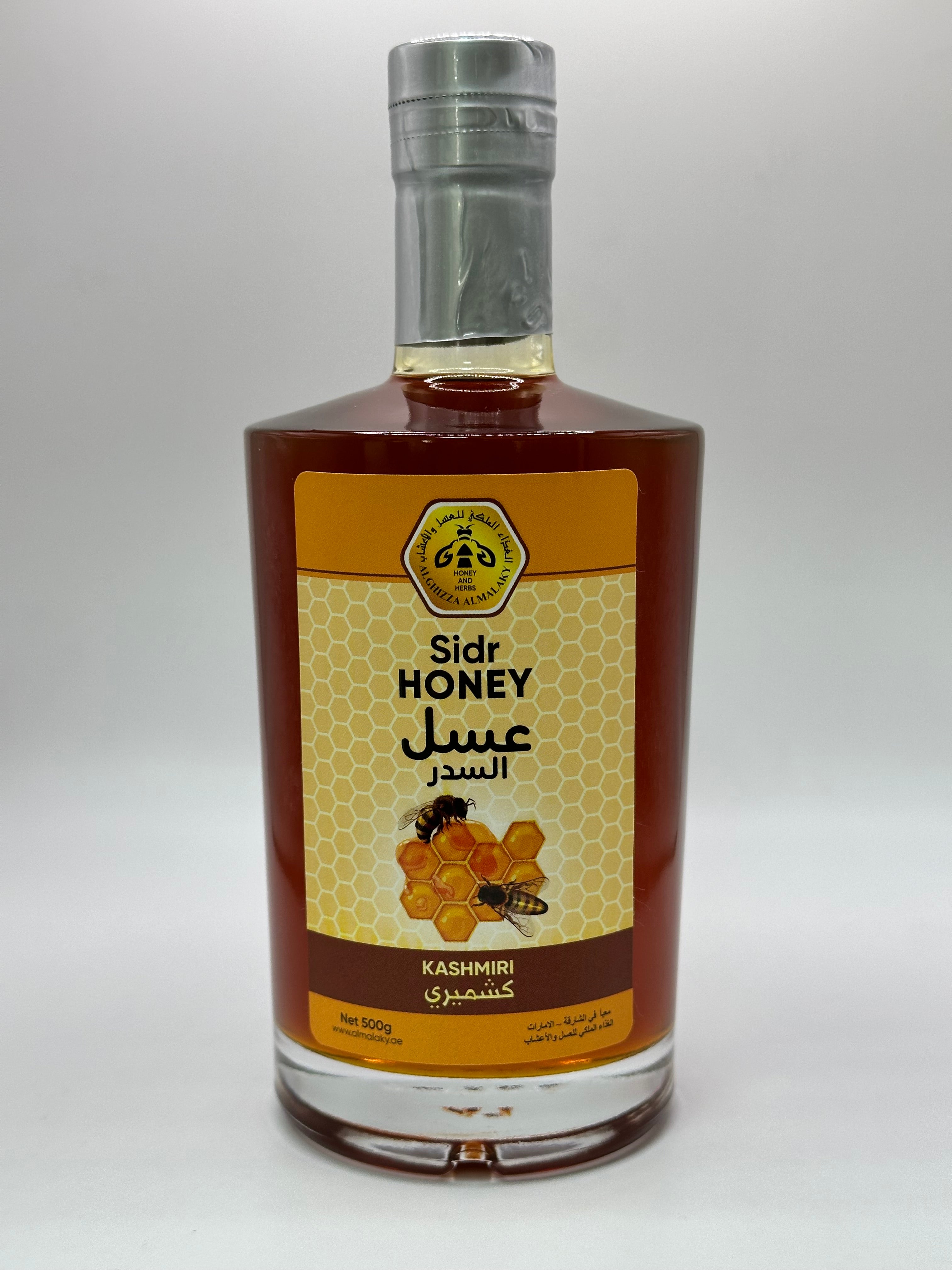 زجاجة عسل السدر الكشميري بحجم 500 غرام، تظهر الزجاجة الطويلة والأنيقة بلونها العنبري الغامق وملصق يحمل اسم المنتج ومنشأه